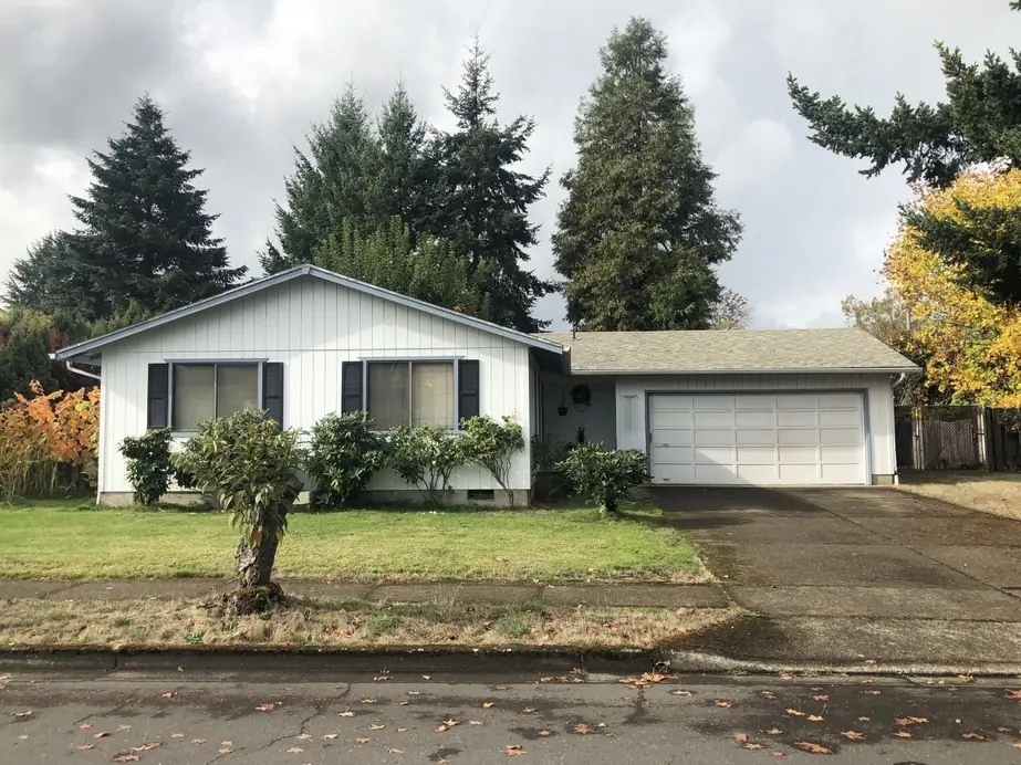 An Oregon ranch house with dark shutters, rhododendrons and a double garage on an autumn day